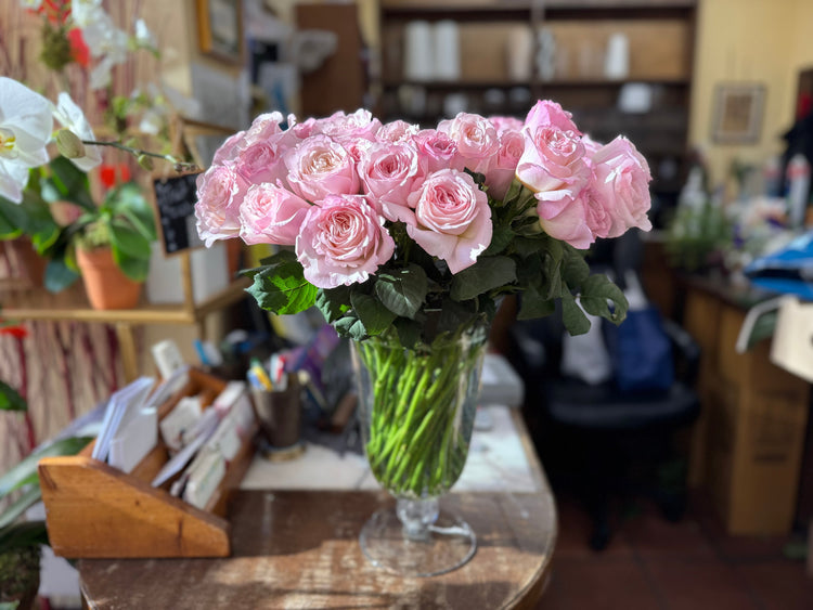 Pink roses in a glass vase beside white and purple orchids inside Jerome Florists' sunlit Upper East Side shop