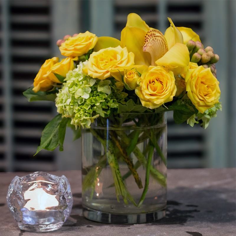 Beautiful yellow roses anchor this arrangement that also includes cymbidium orchid heads and green hydrangea