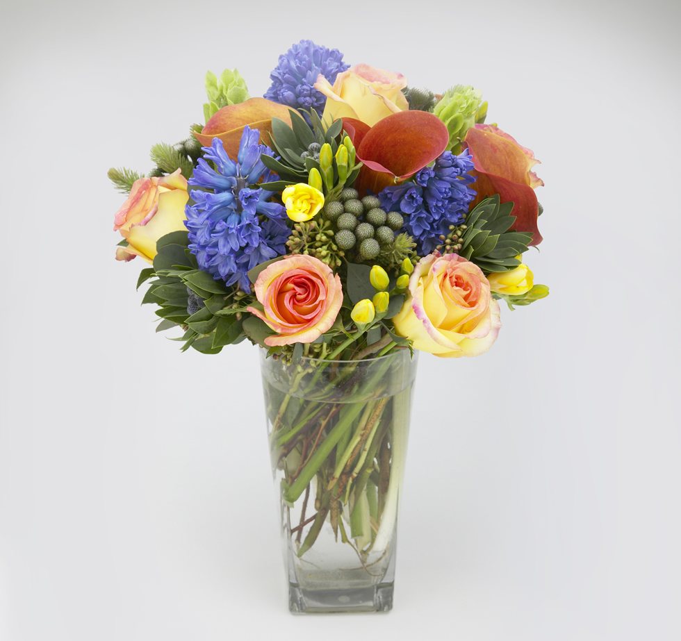 Medley floral arrangement with Ambiance roses, hyacinth, calla lilies, and yellow freesia